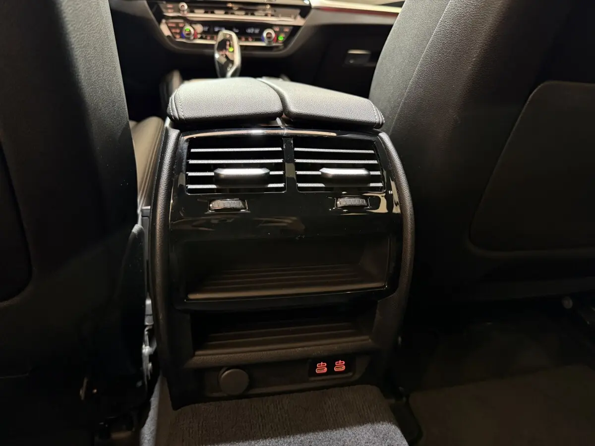 Vue rapprochée de la console centrale arrière noire avec aérateurs et commandes de chauffage sur BMW Série 5 Touring 520d 2023.