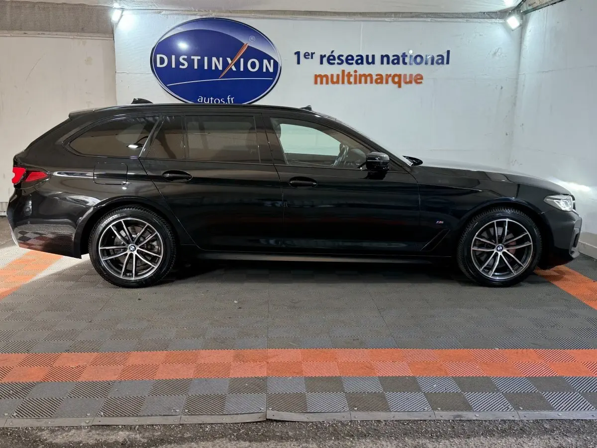 BMW Série 5 Touring 520d M Sport noir vue de profil côté gauche dans un garage avec sol gris et orange.