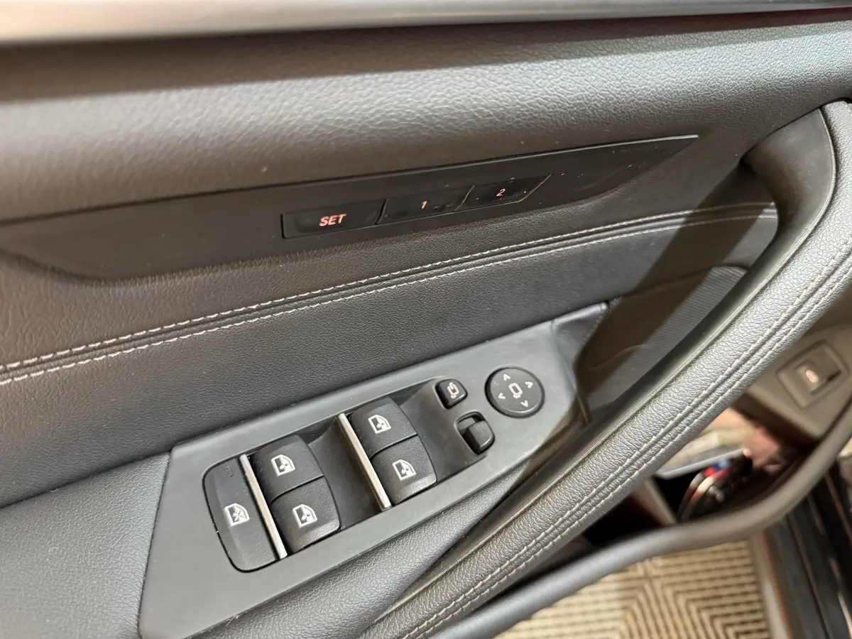 Gros plan sur la commande des vitres et réglages des rétroviseurs côté conducteur d’une BMW Série 5 Touring noire.