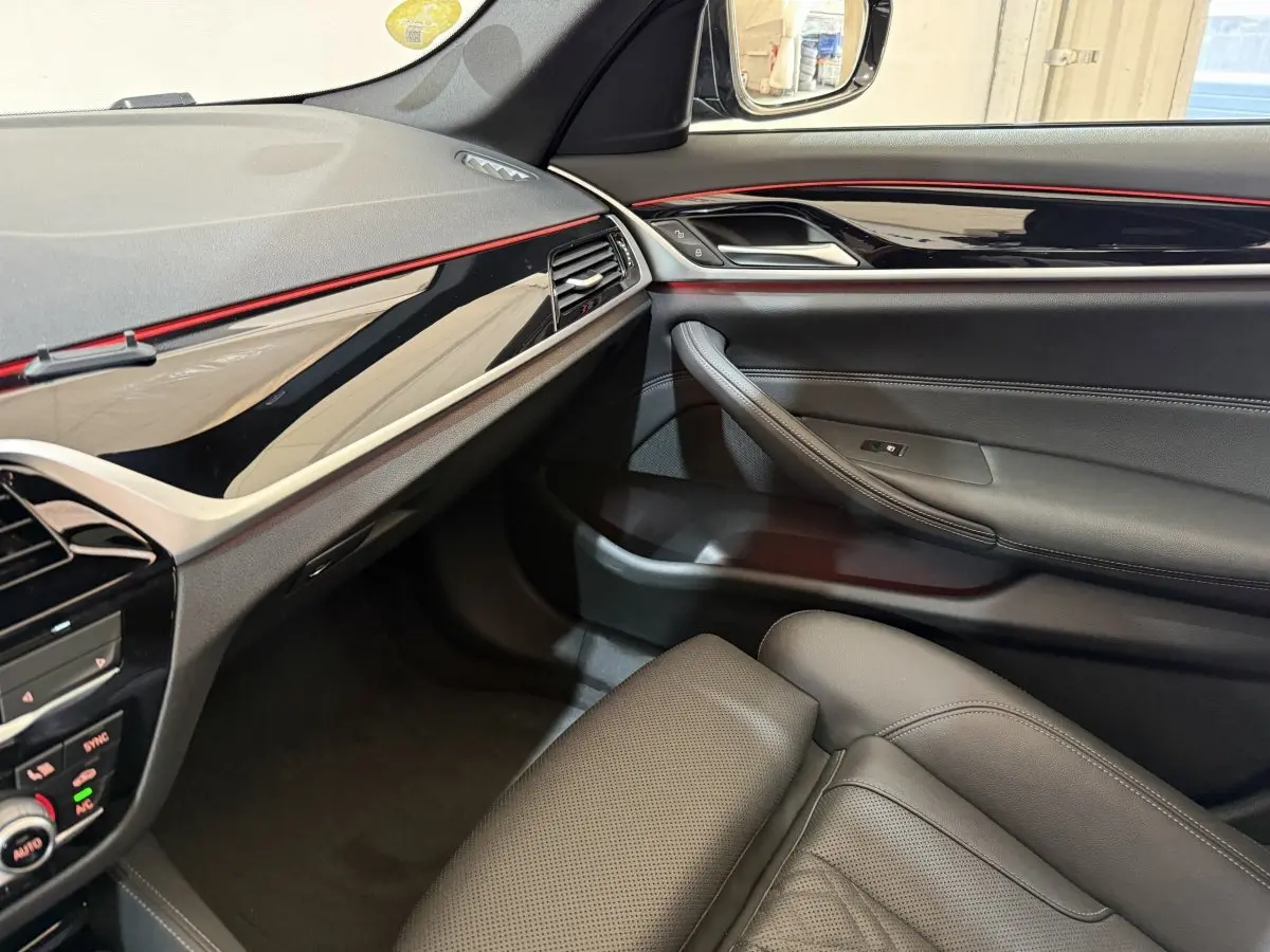 Vue intérieure côté passager de la BMW Série 5 Touring 520d M Sport 2023 avec garnitures noires et bandeau décoratif rouge.