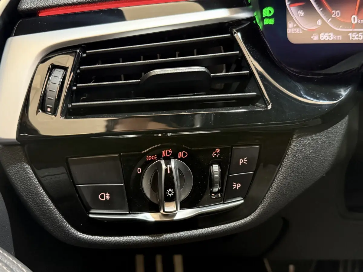 Gros plan sur la commande des phares et la sortie d'air noire du tableau de bord d'une BMW Série 5 Touring 520d 2023.