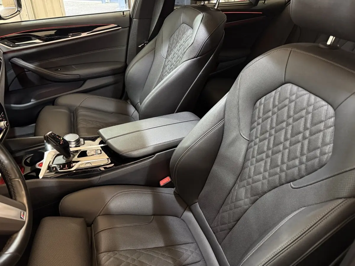 Vue intérieure côté conducteur et passager avant de la BMW Série 5 Touring 520d M Sport, sièges cuir noirs avec surpiqûres.