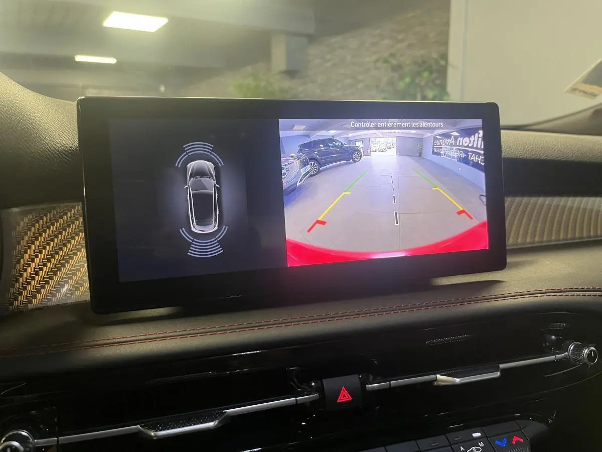Écran central de l'Alfa Romeo Tonale rouge montrant la caméra de recul avec guidage et capteurs de proximité.