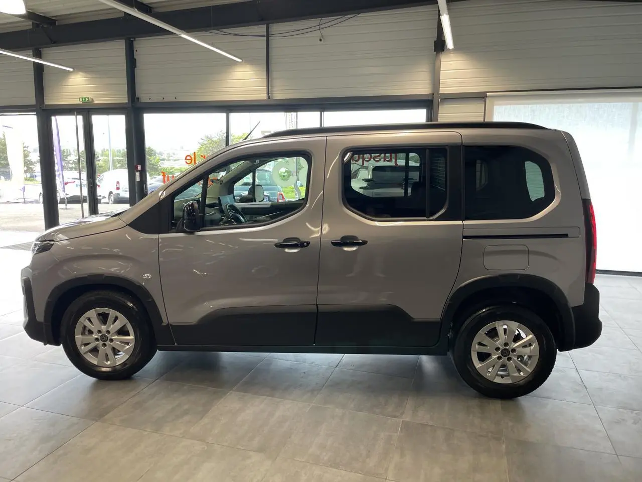 Vue de profil côté gauche du Peugeot Rifter gris Artense avec portes coulissantes et jantes tôles 16 pouces en showroom.