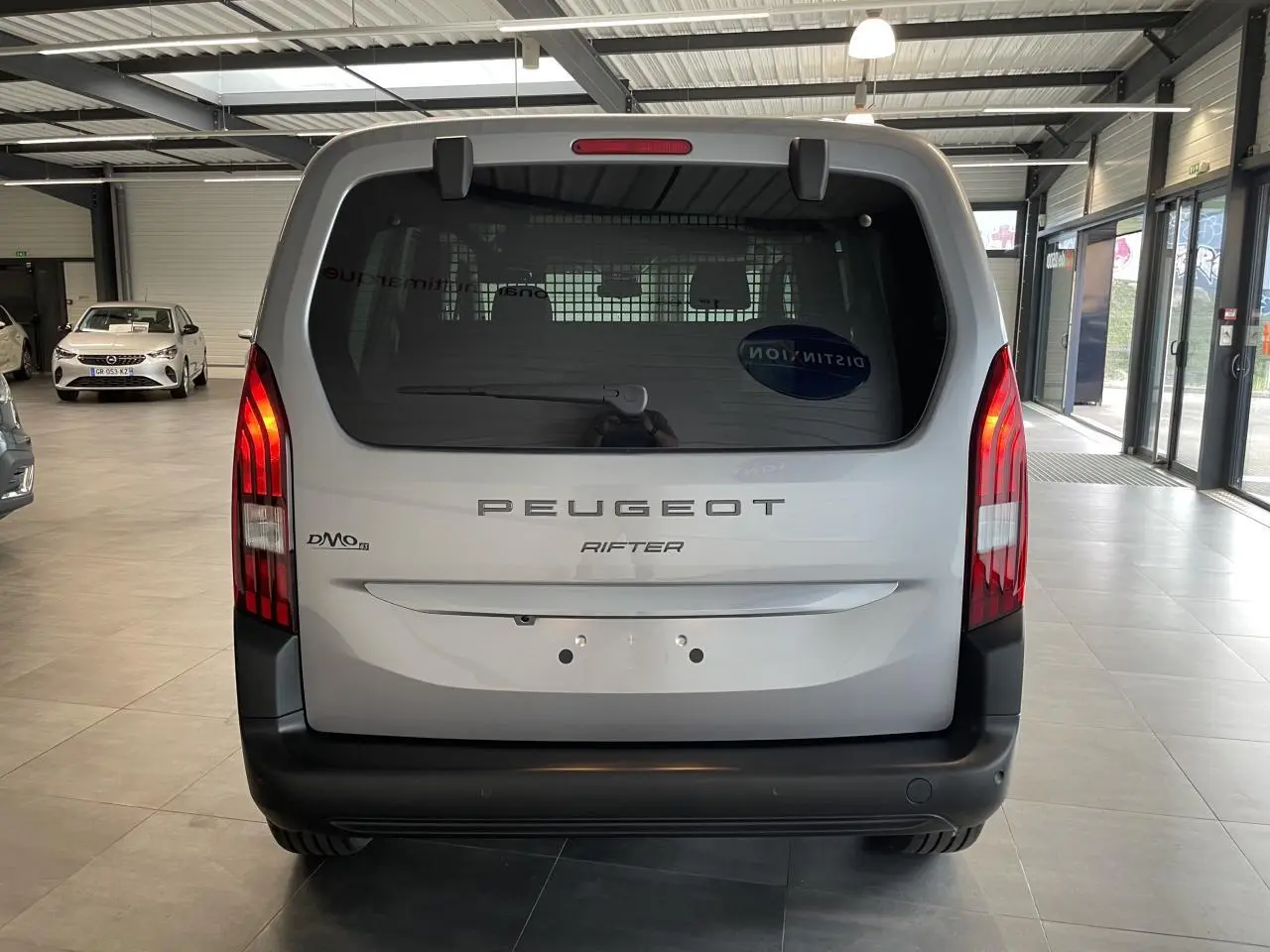 Vue arrière d'un Peugeot Rifter gris Artense avec feux verticaux LED et pare-chocs noir dans un showroom.