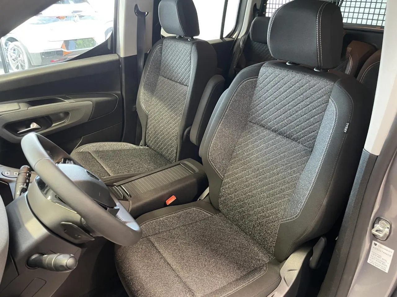 Vue intérieure côté conducteur du Peugeot Rifter gris Artense, mettant en valeur les sièges tissu Sixties et le volant cuir multifonction.