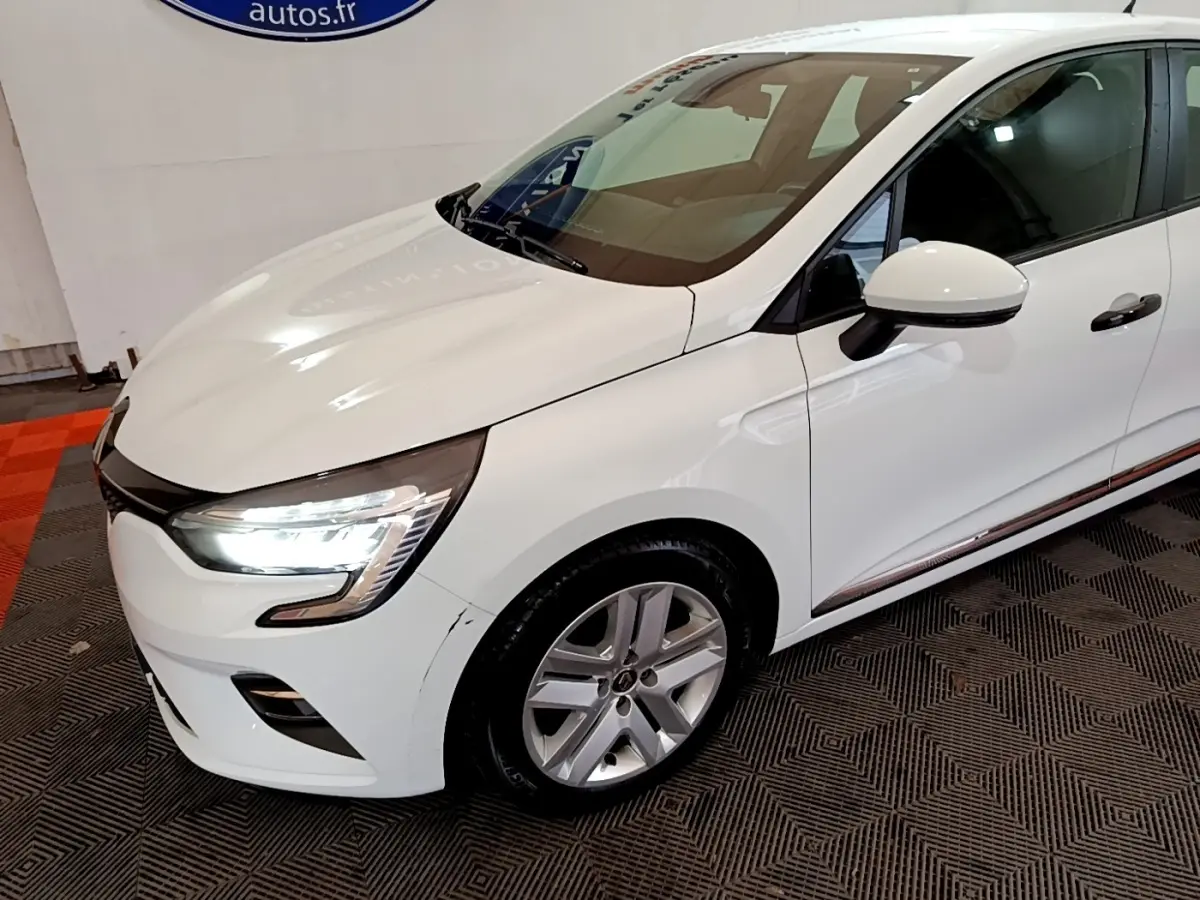 Vue 3/4 avant droit d'une Renault Clio Business blanche avec phares LED allumés et jantes alliage.