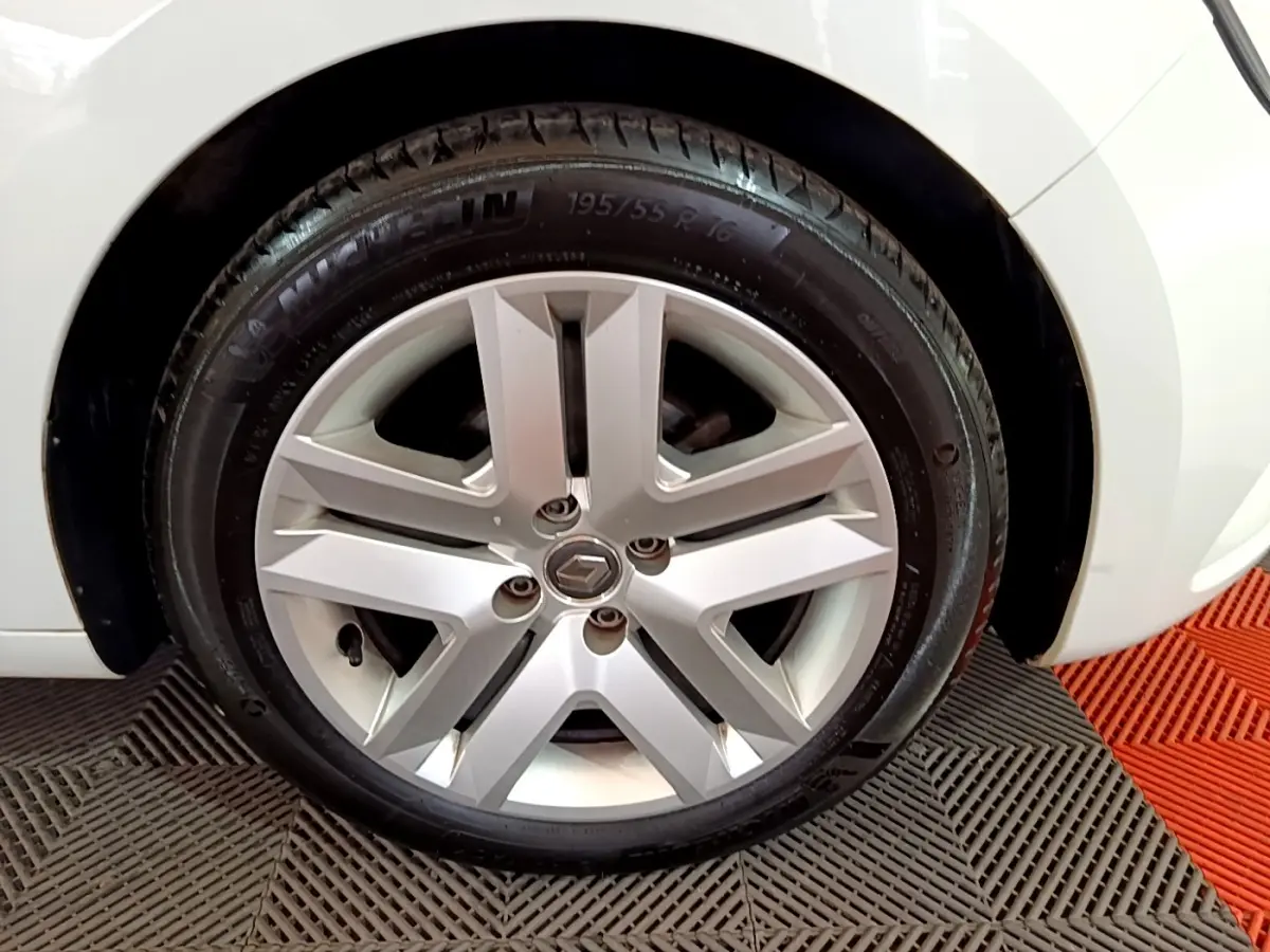 Vue rapprochée de la roue arrière droite d'une Renault Clio Business blanche, sur sol à motifs gris et rouge.