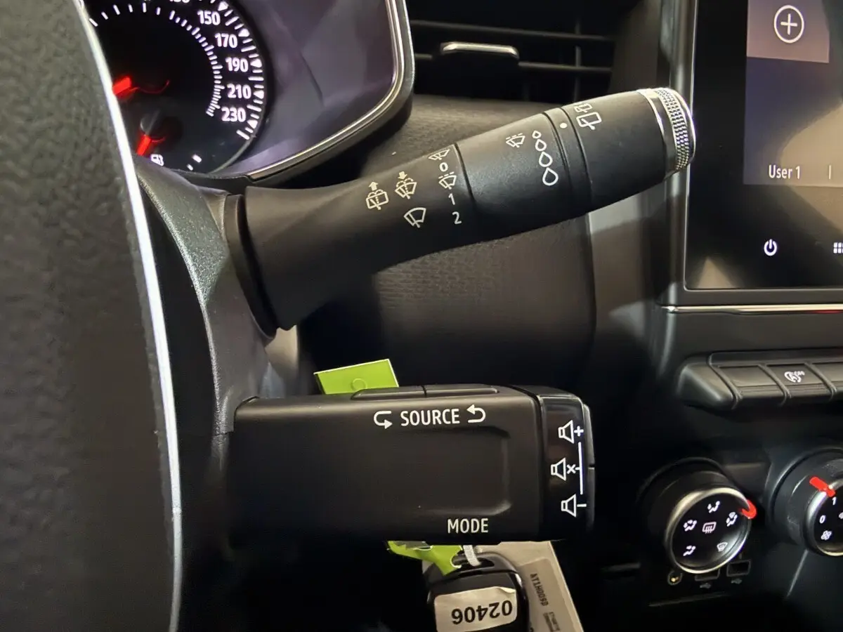 Gros plan sur la commande multifonction noire à gauche du volant d’une Renault Clio Business blanche, tableau de bord partiel visible.