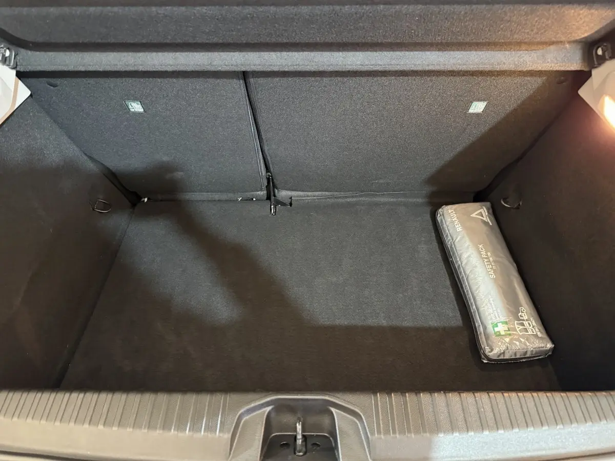 Coffre ouvert vu de dessus d'une Renault Clio Business blanche, avec un kit de sécurité gris posé à droite.