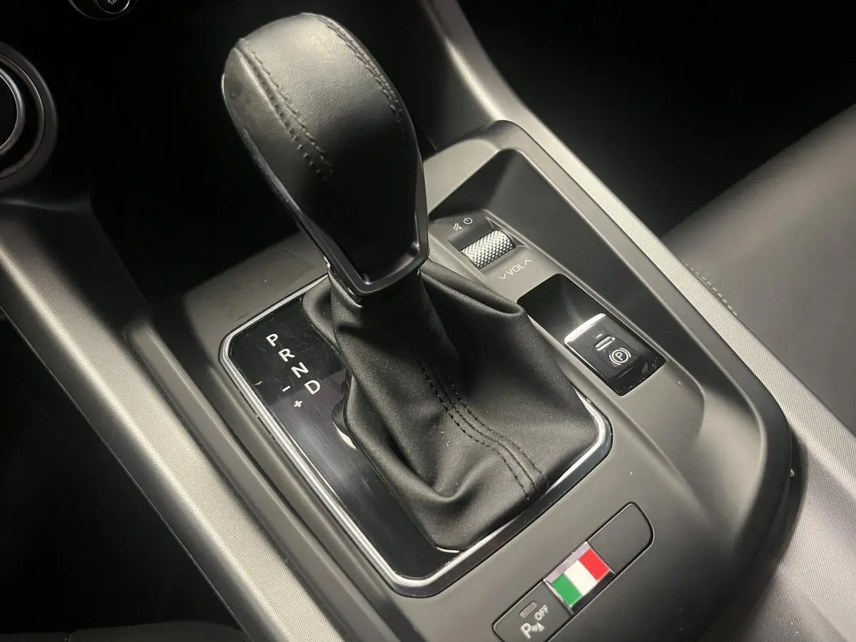 Gros plan sur la console centrale noire de l'Alfa Romeo Tonale avec levier de vitesse automatique et badge tricolore italien.