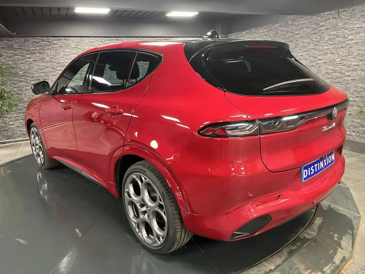 Vue 3/4 arrière droite de l'Alfa Romeo Tonale rouge avec jantes alliage 20 pouces et toit noir en intérieur showroom.