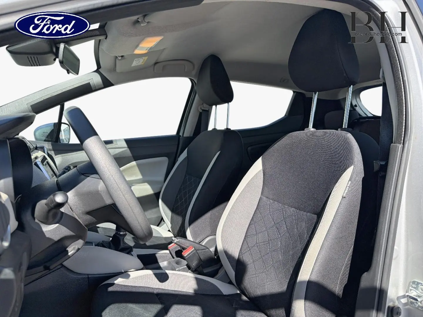 Vue intérieure côté conducteur d'une Nissan Micra 2017 avec sièges tissu noir et gris, volant multifonction et boîte manuelle.
