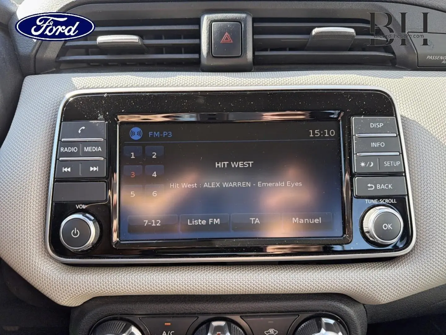 Tableau de bord beige avec écran tactile central et commandes média, intérieur d'une Nissan Micra vue de face.