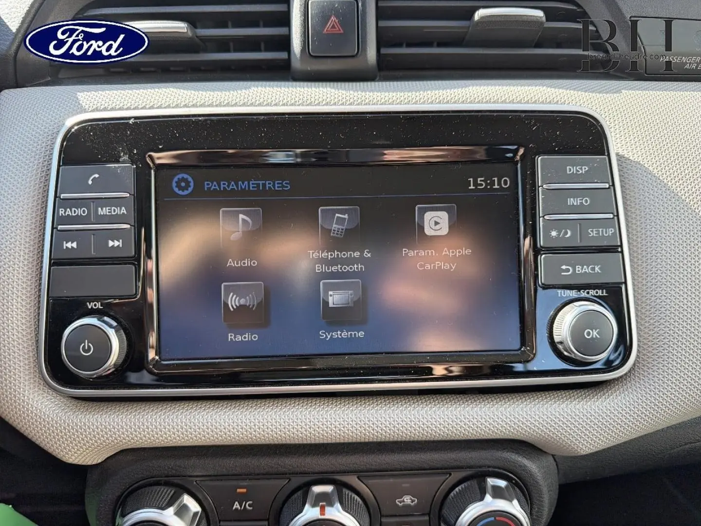 Écran tactile central noir avec commandes autour, tableau de bord beige clair de Nissan Micra 2017, vue frontale rapprochée.