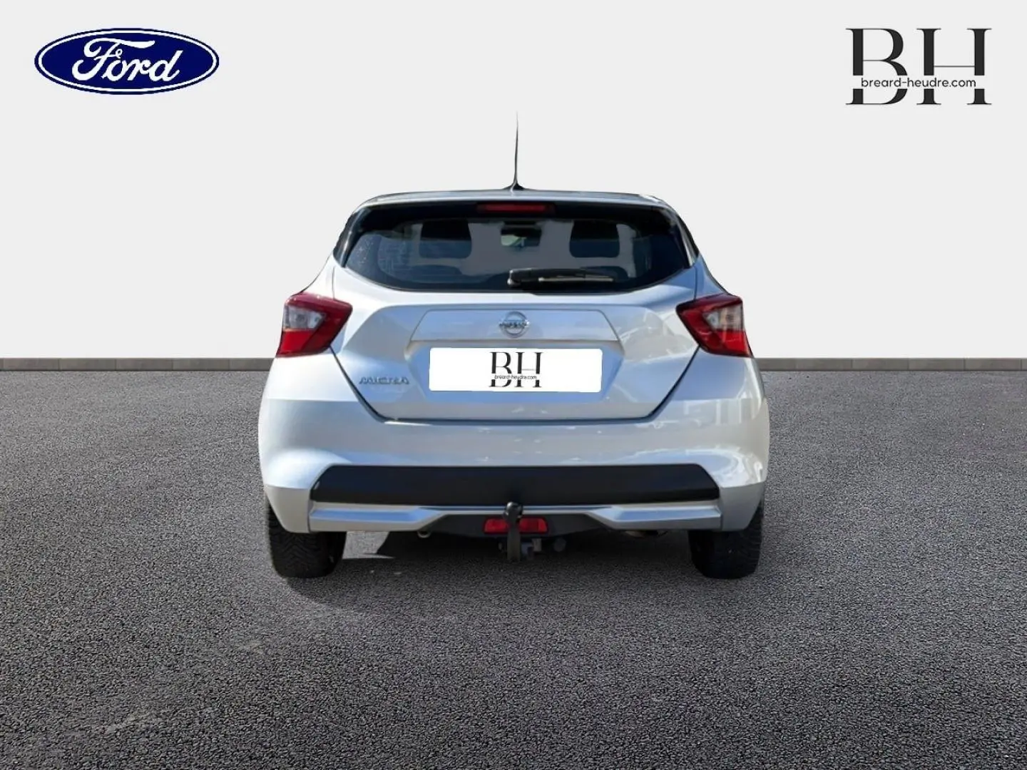 Vue arrière d'une Nissan Micra blanche 2017 avec attelage et feux arrière rouges sur fond neutre.