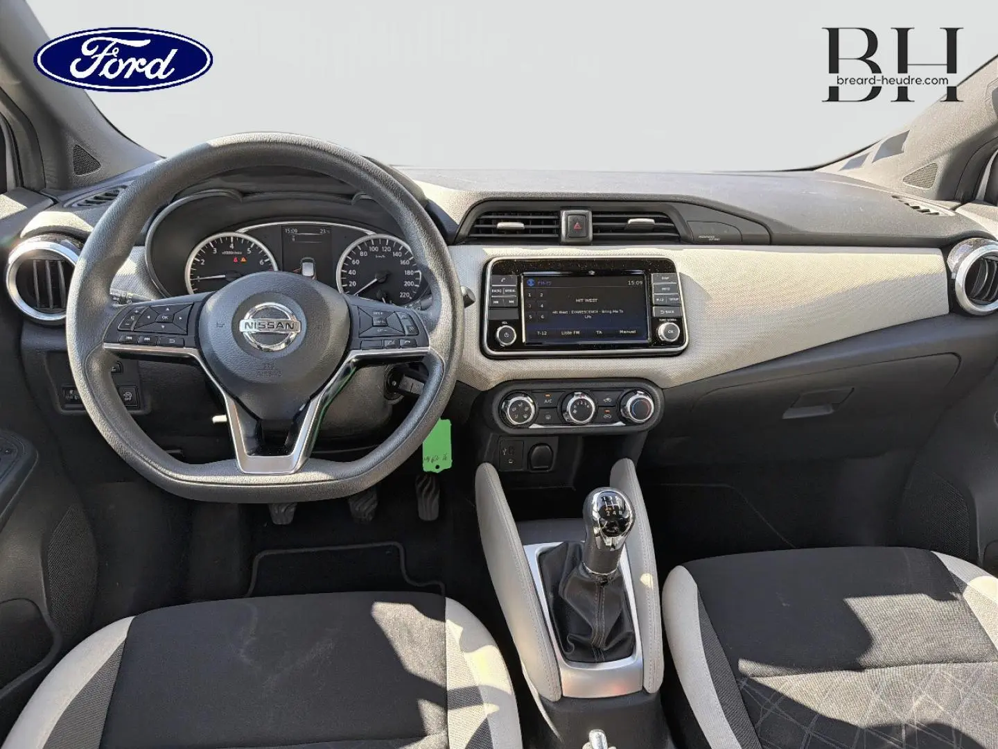 Vue intérieure avant centrée sur le tableau de bord et volant Nissan d'une Micra 2017, avec levier de vitesse manuel et sellerie bicolore.