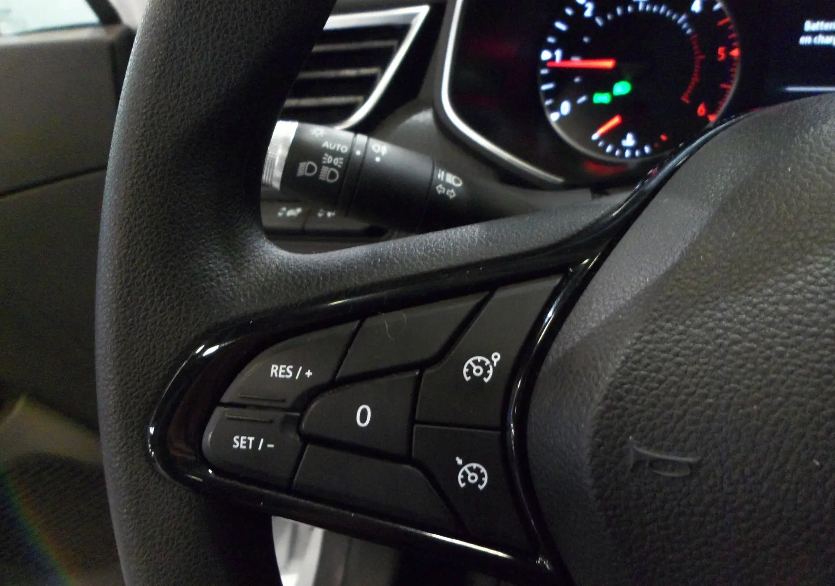 Gros plan sur les commandes de régulateur de vitesse au volant d'une Renault Clio V blanche Glacier, tableau de bord en arrière-plan.