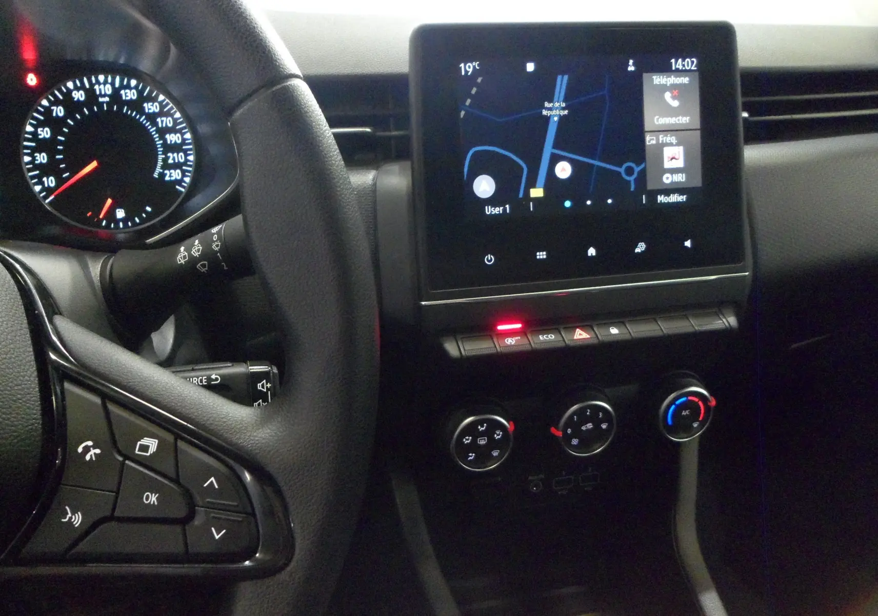 Intérieur de la Renault Clio V blanche, vue du tableau de bord avec écran tactile et commandes climatisation visibles.