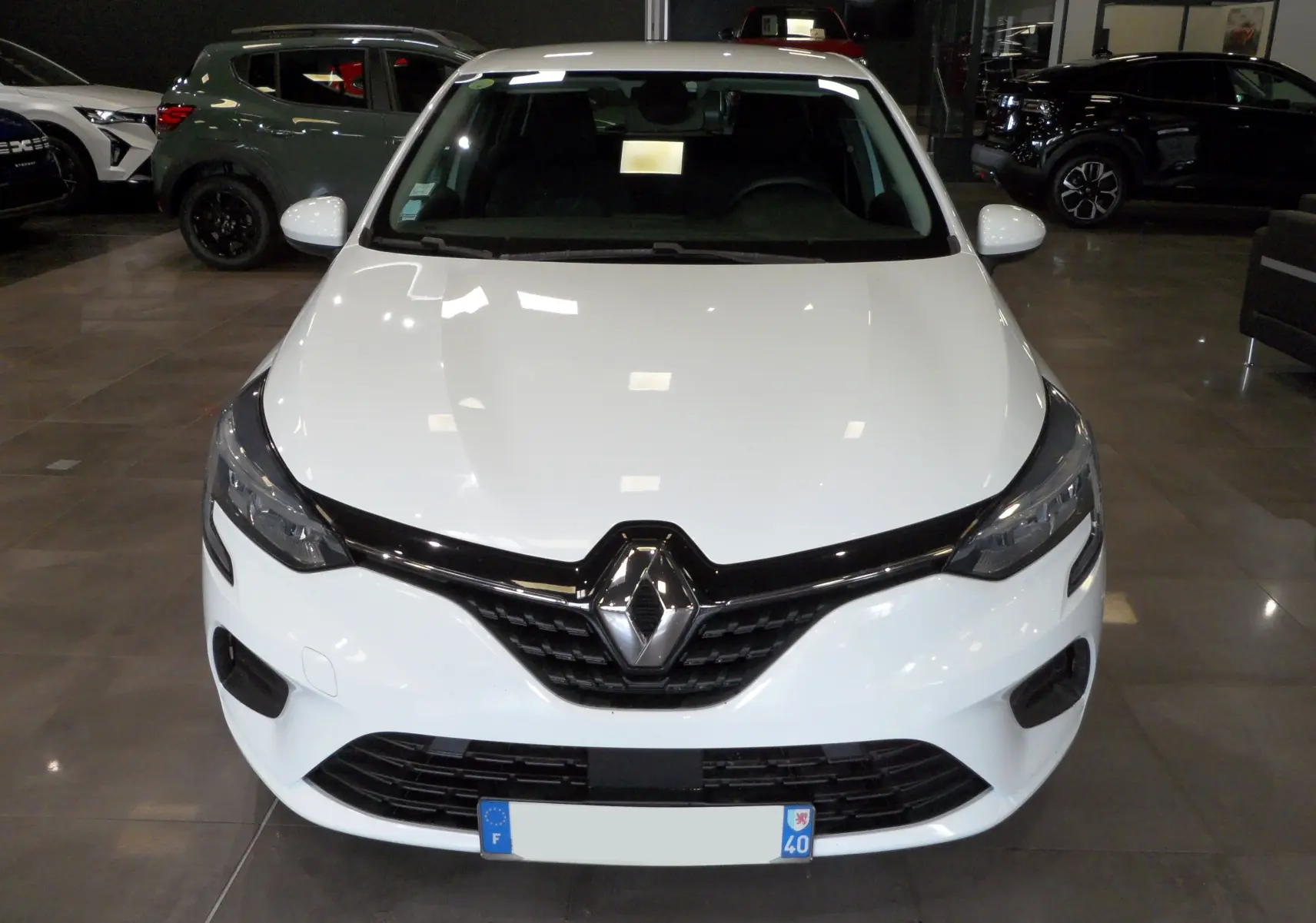 Vue frontale d'une Renault Clio V blanche Glacier en showroom, soulignant sa calandre noire et ses phares modernes.