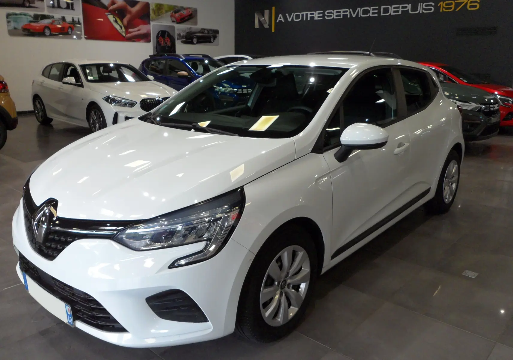 Renault Clio V blanche vue en 3/4 avant droit dans un showroom avec phares et calandre noirs.