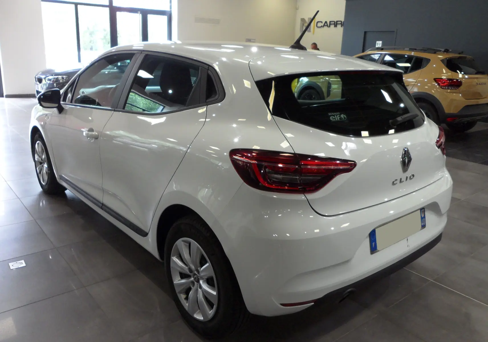 Vue 3/4 arrière droite d'une Renault Clio V blanche Glacier en showroom, avec feux arrière LED et jantes alliage.