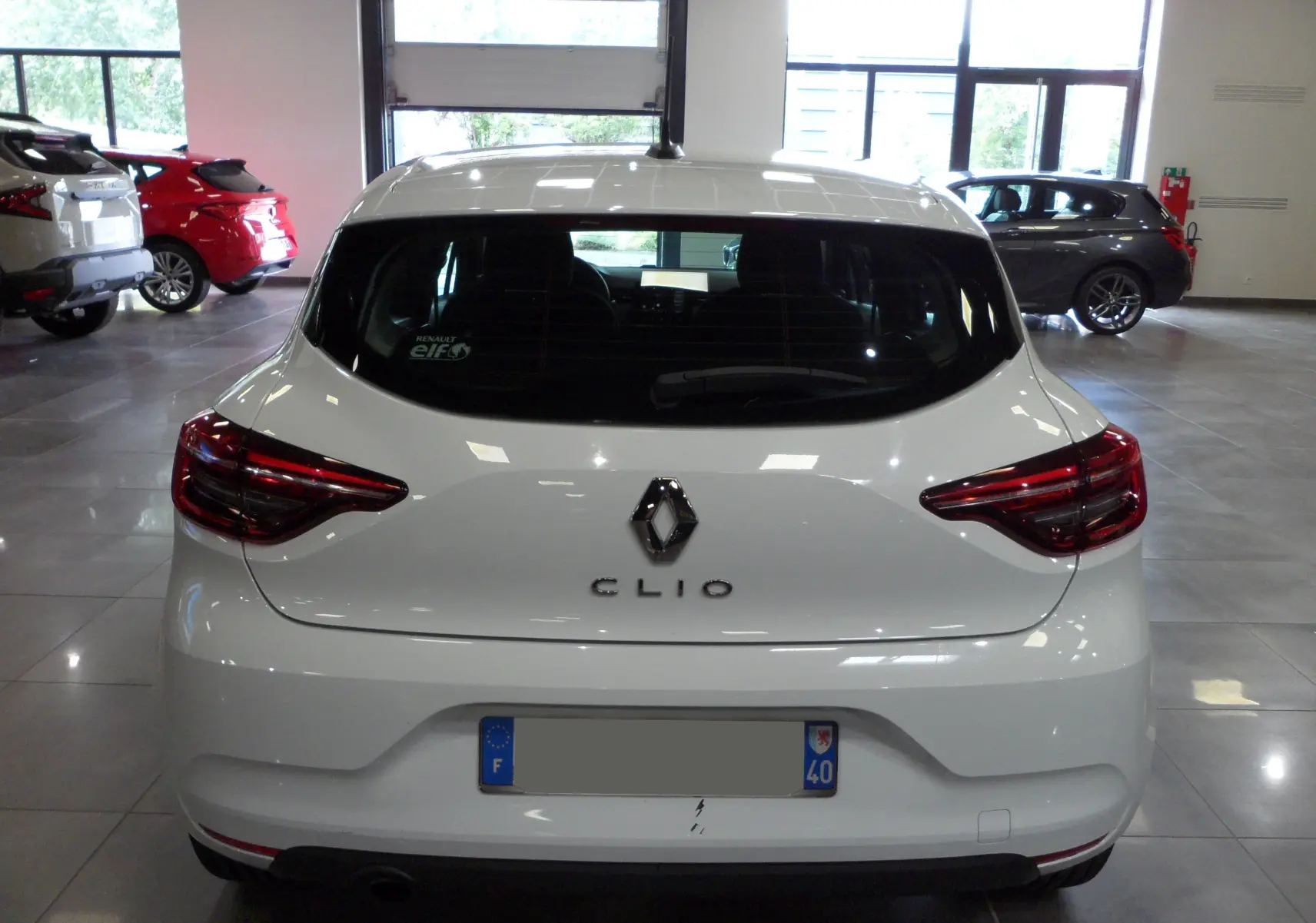 Vue arrière d'une Renault Clio V blanche Glacier en intérieur, avec feux arrière LED et logo central visible.