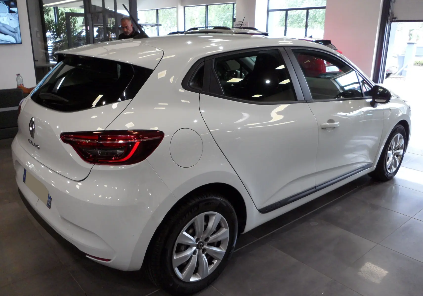 Vue 3/4 arrière droite d'une Renault Clio V blanche Glacier en intérieur, avec feux arrière LED et jantes alliage.