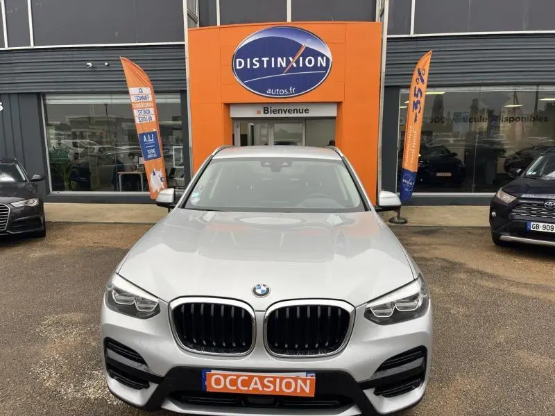 Vue avant d'un BMW X3 xDrive30eA 2020 Glacier Silver avec calandre double haricot et plaque "OCCASION" devant un concessionnaire.