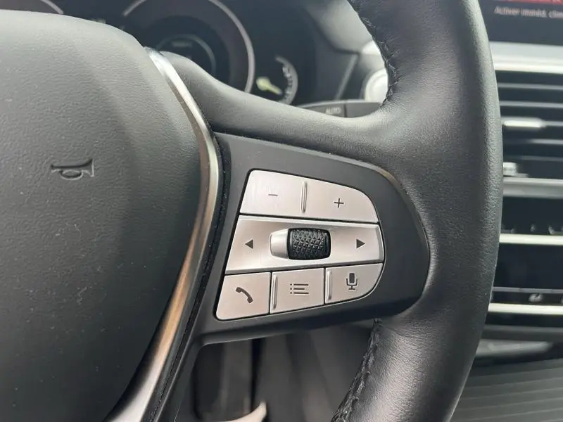Gros plan sur les commandes argentées au volant cuir noir d'une BMW X3 xDrive30eA 2020, intérieur moderne.