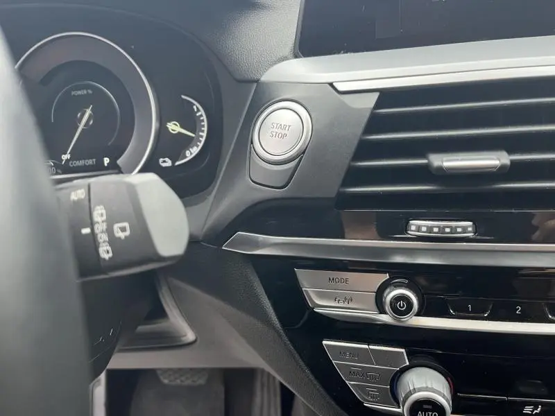 Détail intérieur côté gauche du tableau de bord BMW X3 xDrive30eA 2020 avec bouton Start/Stop et commandes climatisation.