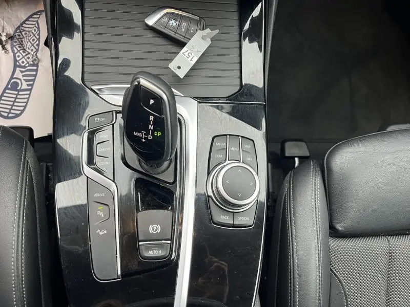 Vue plongeante sur la console centrale noire brillante du BMW X3 xDrive30e, avec levier de vitesses et commandes multimédia.