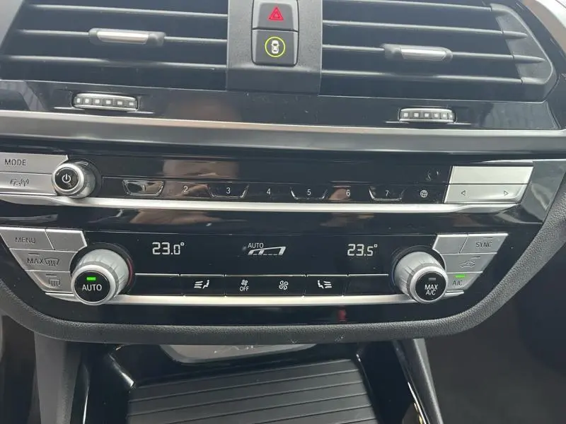 Vue rapprochée de la console centrale noire du BMW X3 xDrive30e 2020, affichant la climatisation automatique tri-zone.