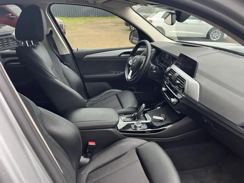 Vue intérieure côté conducteur de la BMW X3 xDrive30eA 2020, sièges noirs et tableau de bord moderne avec écran tactile.