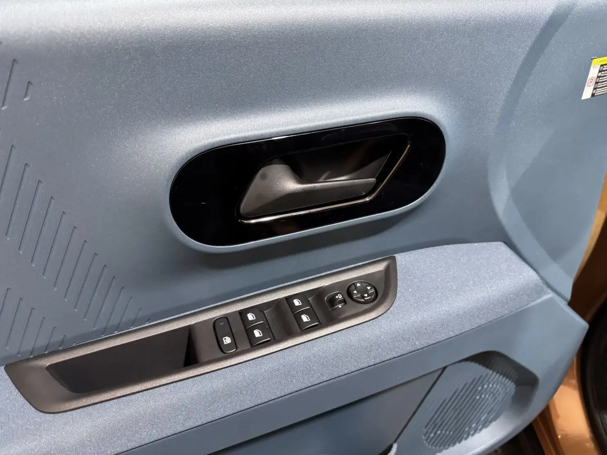 Gros plan sur la porte côté conducteur marron de la Fiat Grande Panda avec poignée noire et commandes électriques.