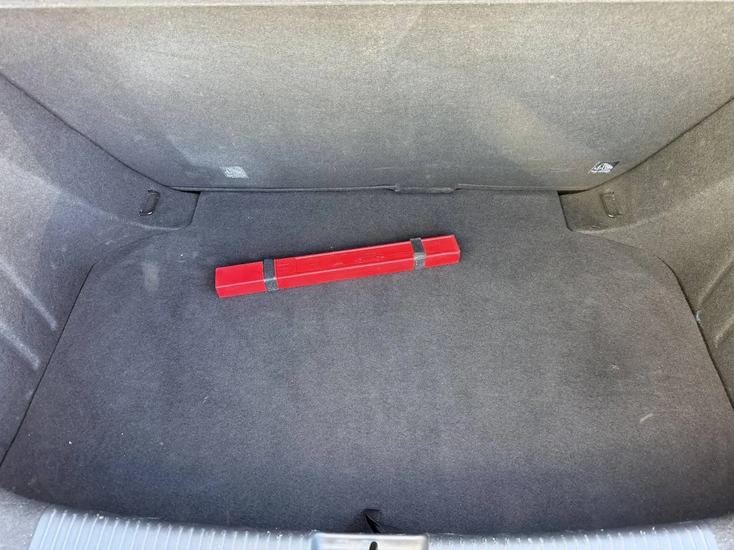 Coffre ouvert de MG3 1.5 Hybrid+ 2024 en Pebble Black, avec tapis noir et triangle de signalisation rouge posé au centre.