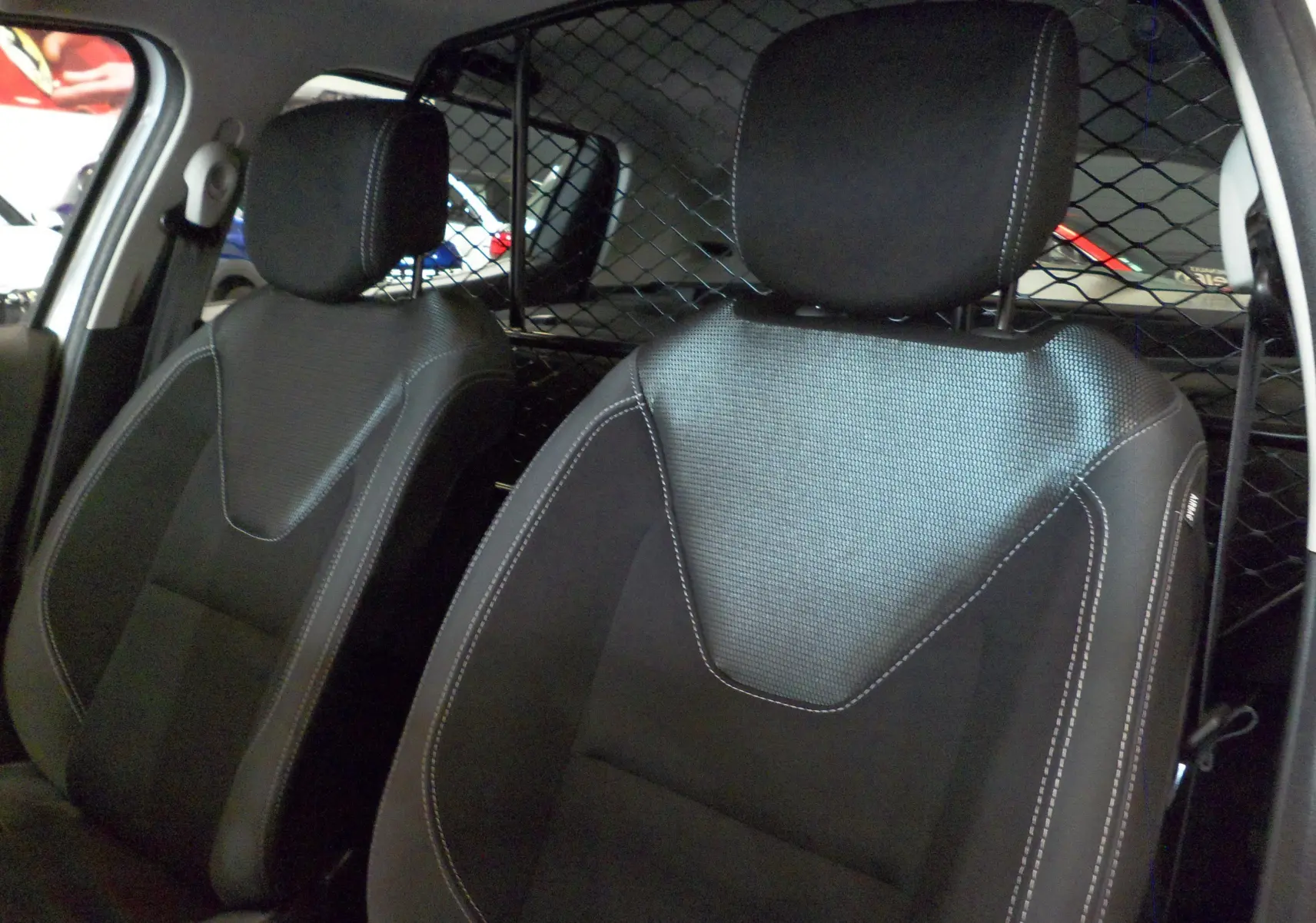 Gros plan sur les sièges avant noirs en tissu avec surpiqûres blanches de la Renault Clio IV Société blanche, séparés par une grille métallique.