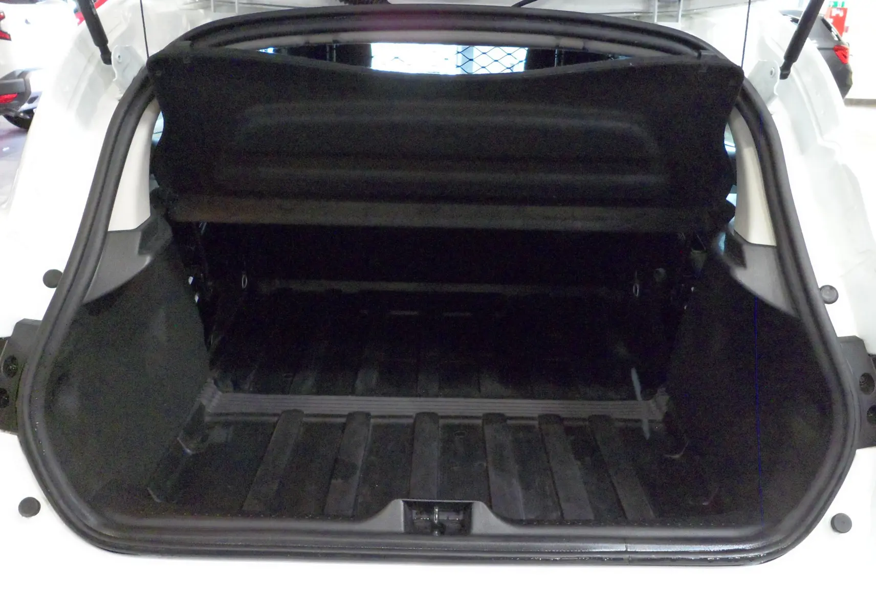 Coffre ouvert vu de l'arrière d'une Renault Clio IV Société blanc glacier, montrant l'espace de chargement vide.