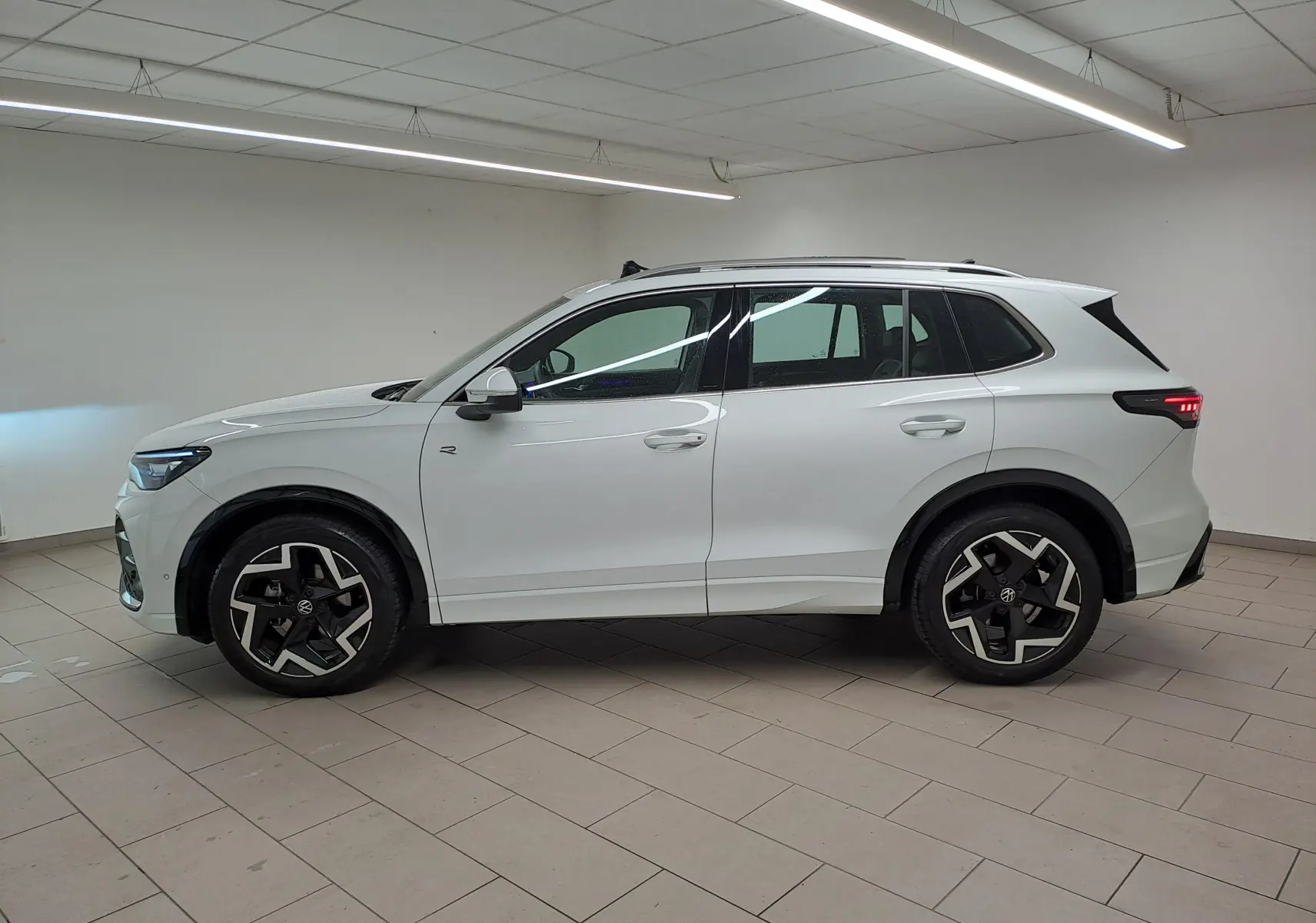 Vue de profil côté gauche du Volkswagen Tiguan blanc pur 2025, finition R-Line avec jantes distinctives noires et argentées.