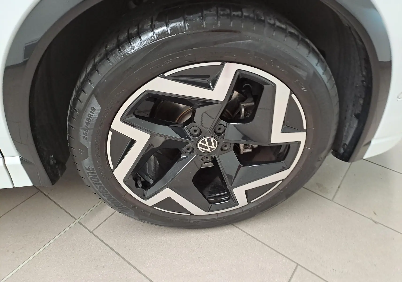 Gros plan sur la roue avant gauche du Volkswagen Tiguan blanc Pur, avec jante alliage noire et argentée au design géométrique.