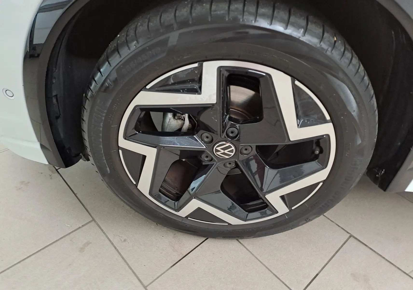 Gros plan sur la roue avant gauche du Volkswagen Tiguan blanc pur, avec jante alliage noire et argentée au design moderne.