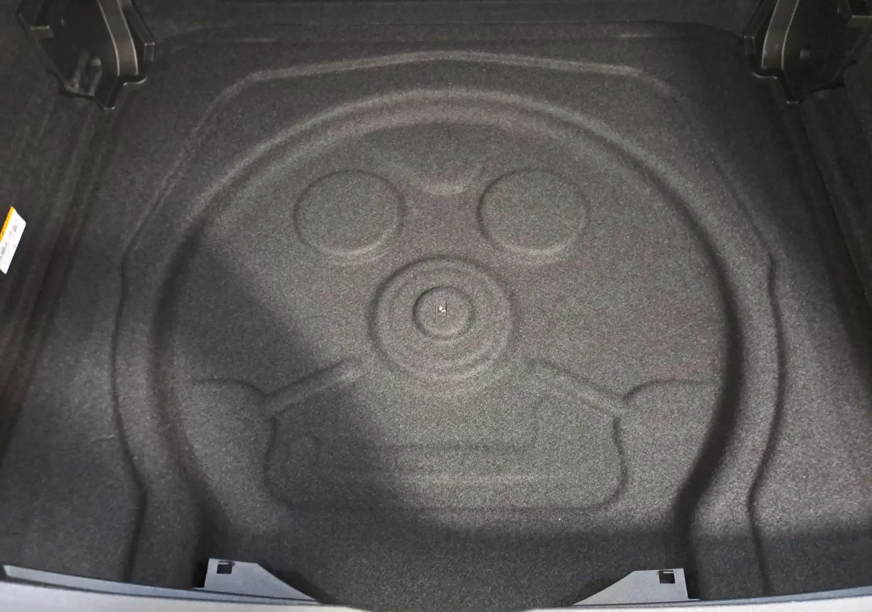 Coffre ouvert du Volkswagen Tiguan blanc pur 2025, vue plongeante sur l'espace de rangement sans roue de secours visible.