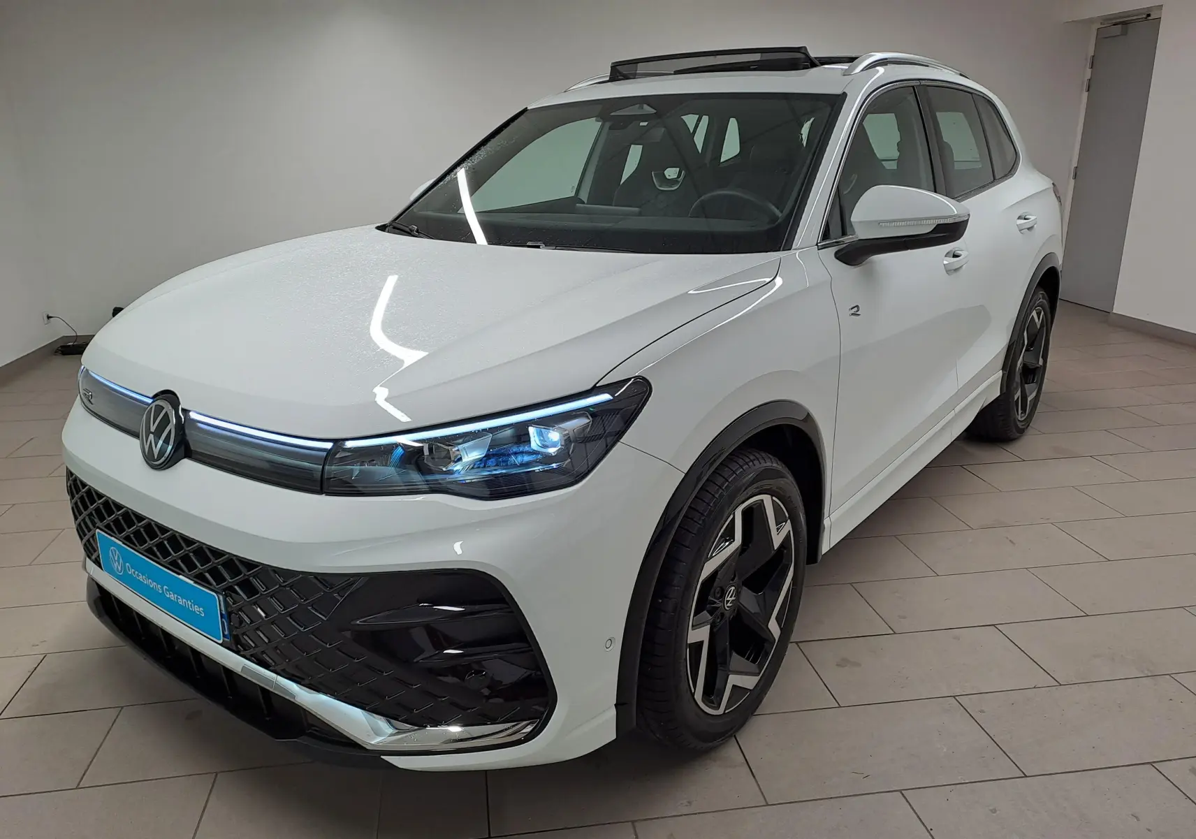 Vue 3/4 avant droite du Volkswagen Tiguan blanc pur 2025, finition R-Line avec jantes noires distinctives.