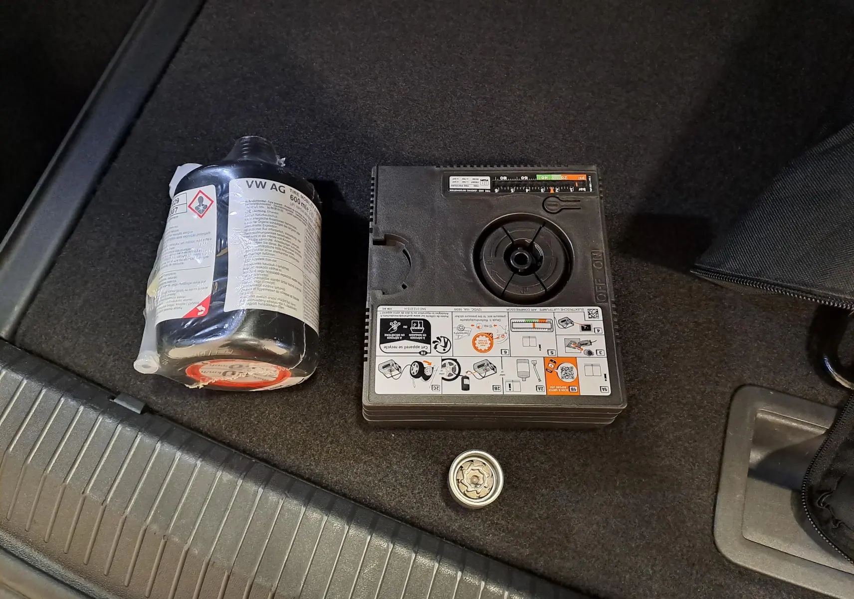 Image du coffre d’un Volkswagen Tiguan blanc pur, montrant un kit de réparation pneu avec compresseur et produit d’étanchéité.