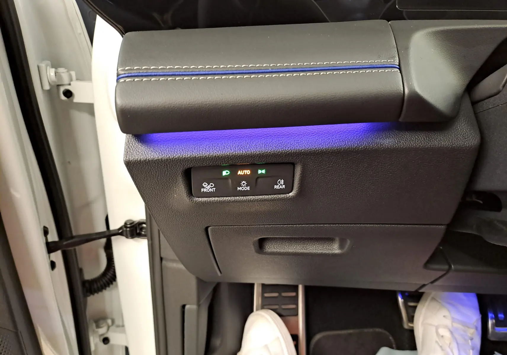 Vue intérieure côté conducteur du Volkswagen Tiguan blanc pur 2025, avec éclairage d'ambiance bleu et commandes des phares visibles.