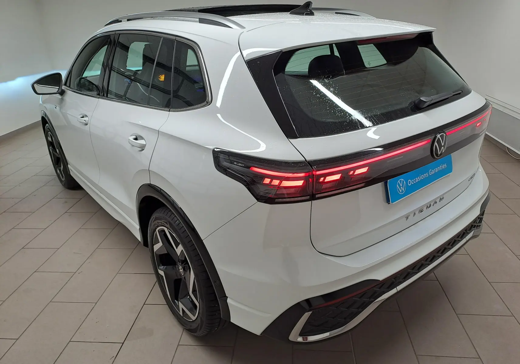 Vue 3/4 arrière droite du Volkswagen Tiguan blanc pur 2025 avec feux arrière LED allumés et jantes noires distinctives.