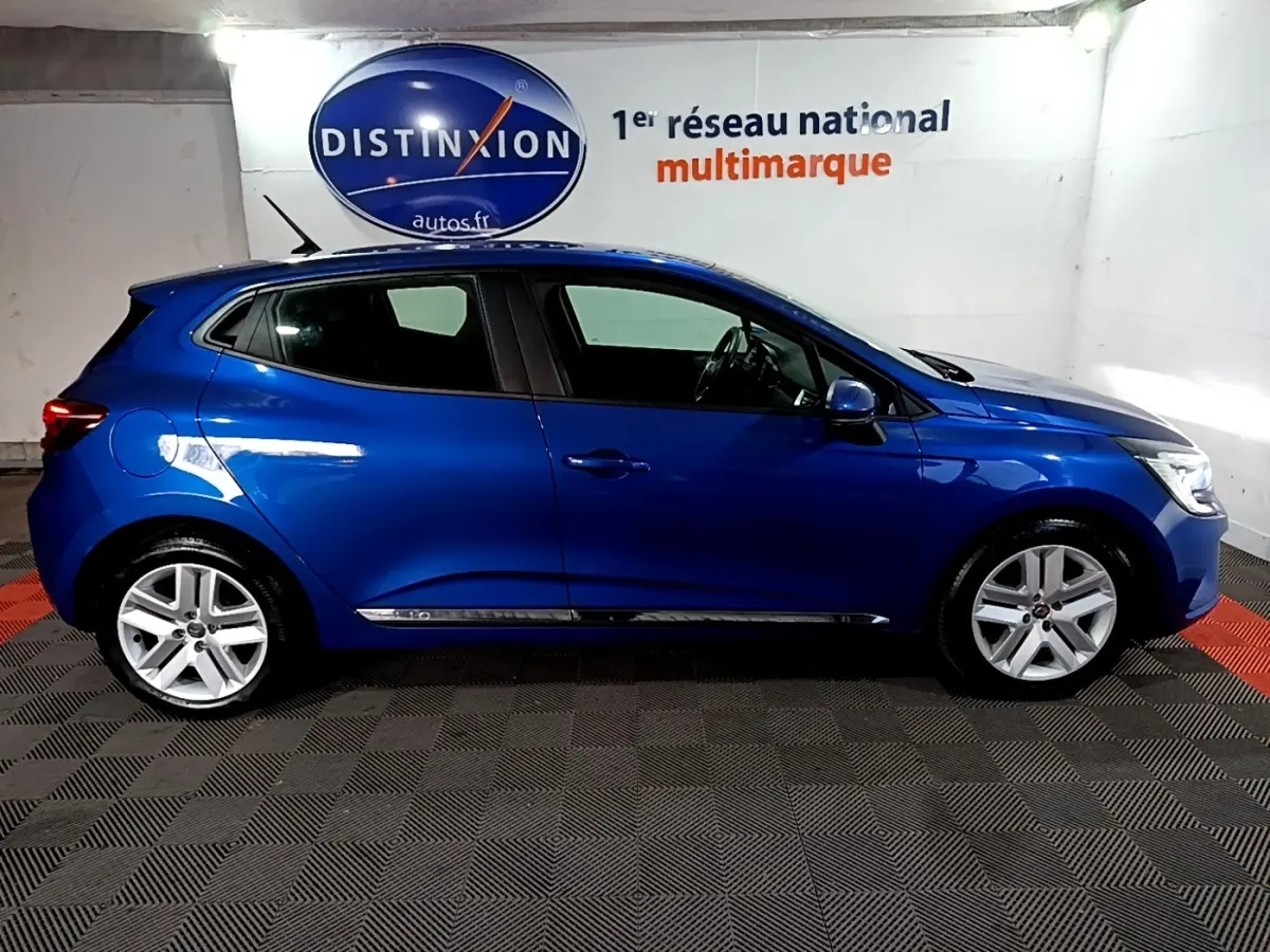 Vue latérale droite d'une Renault Clio Business bleu métallisé, stationnée en intérieur avec jantes alliage visibles.