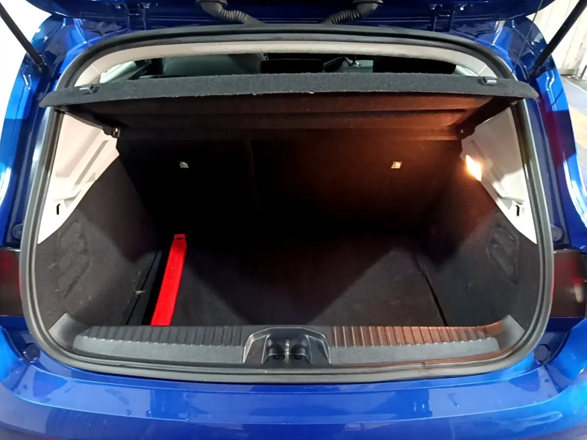 Coffre ouvert vu de l'arrière d'une Renault Clio Business bleu, avec tapis noir et lumière intérieure allumée.