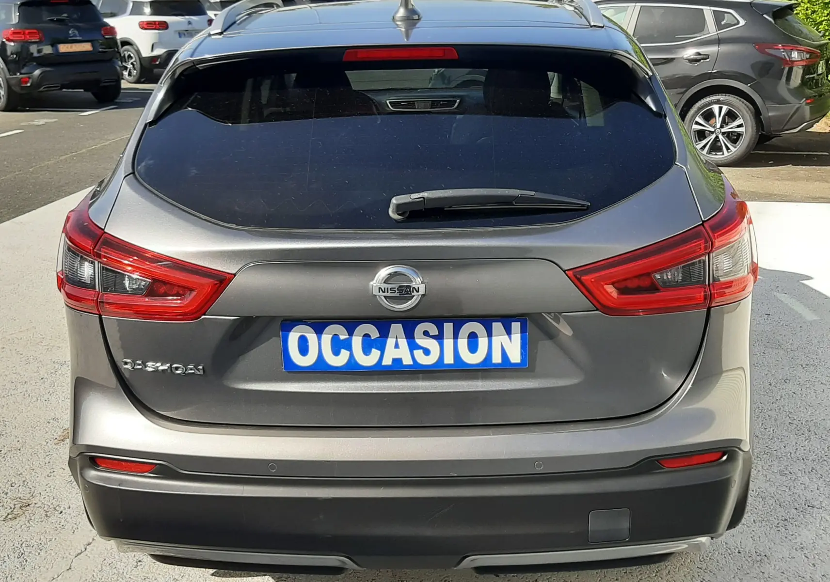 Vue arrière d'un Nissan Qashqai marron métal 2018 avec plaque "OCCASION" sur un parking extérieur.