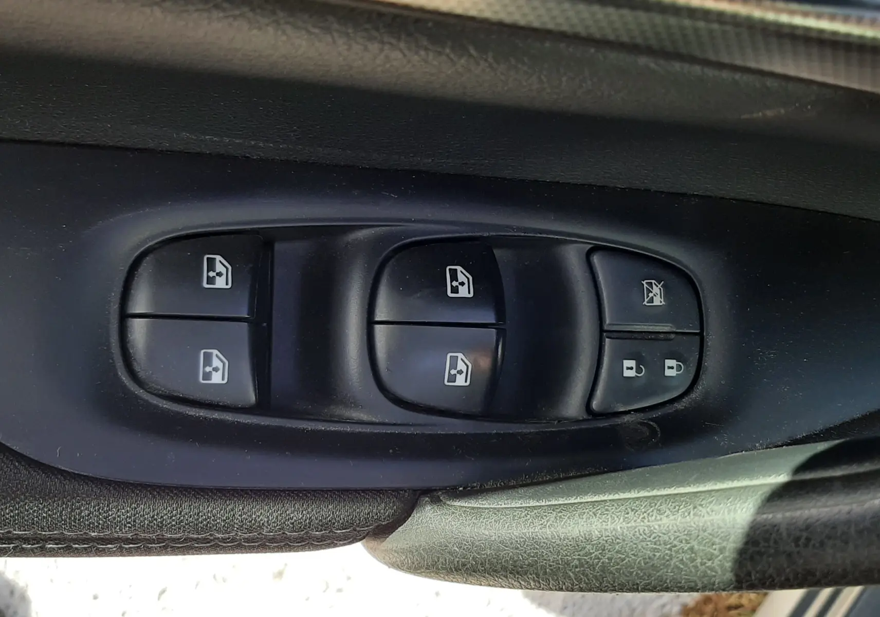 Gros plan sur les commandes des vitres électriques côté conducteur d’un Nissan Qashqai marron métal 2018.
